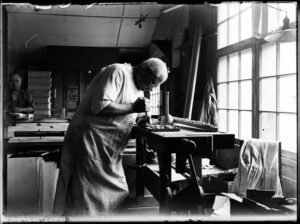 Craftsperson hand-finishing furniture in a historic workshop during the early development of Finnish design.